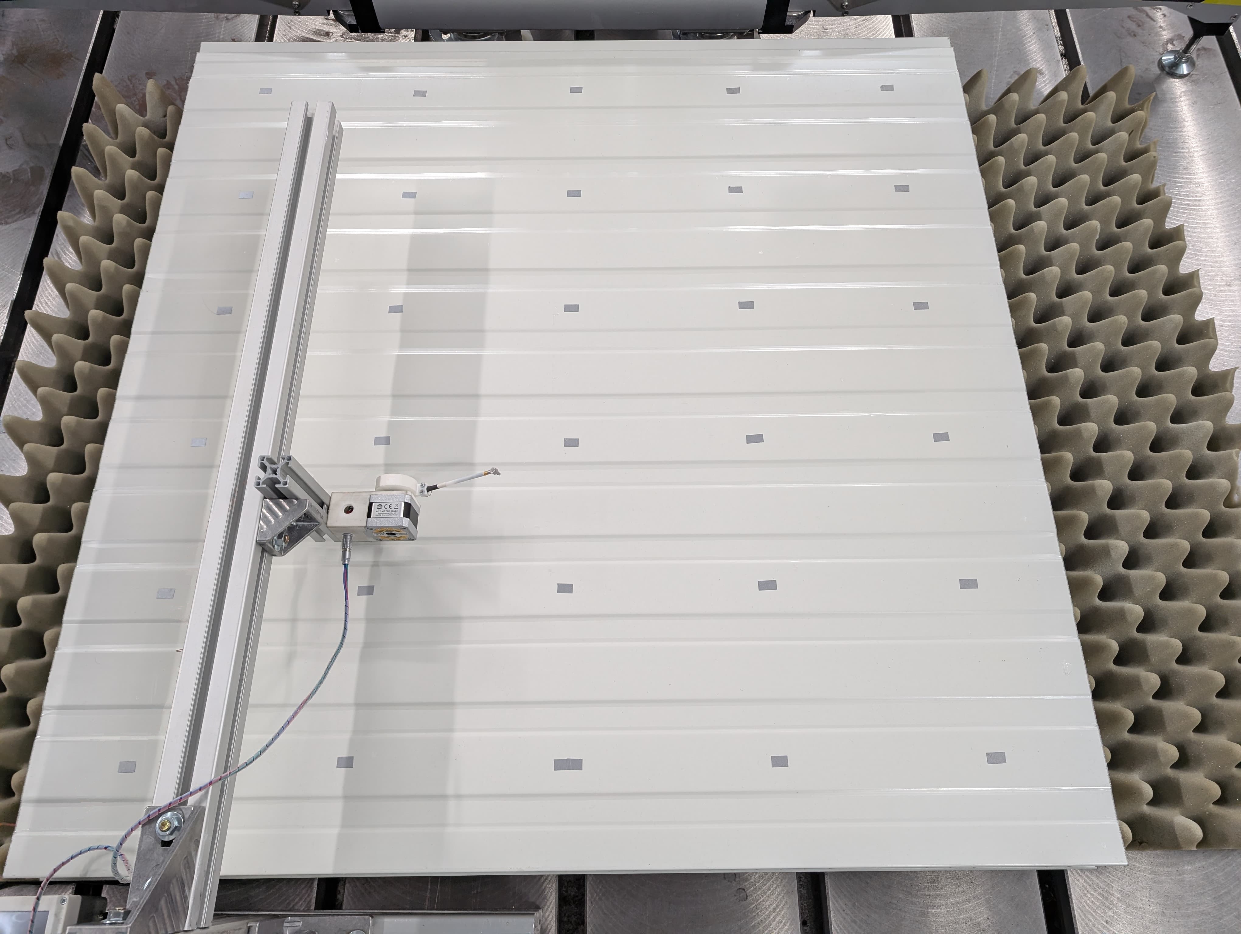 Versuchsaufbau mit automatischem Modalhammer, Sandwichelement und markierten Messpunkten für das Laser-Doppler-Vibrometer 